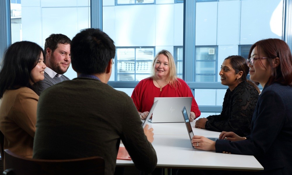 Six people sitting around a table at a meeting.